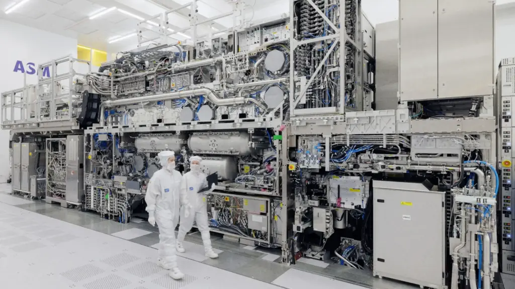 Interno di una fabbrica TSMC: due operatori camminano tra enormi macchinari.