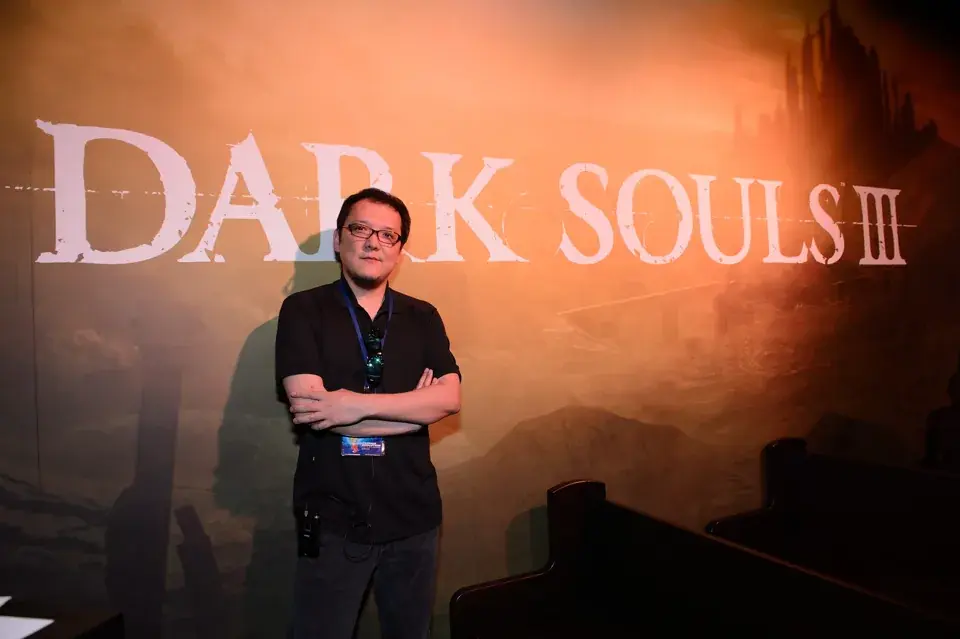 Hidetaka Miyazaki posa sullo sfondo di Dark Souls III, uno dei titoli più iconici e di successo sviluppati da FromSoftware.